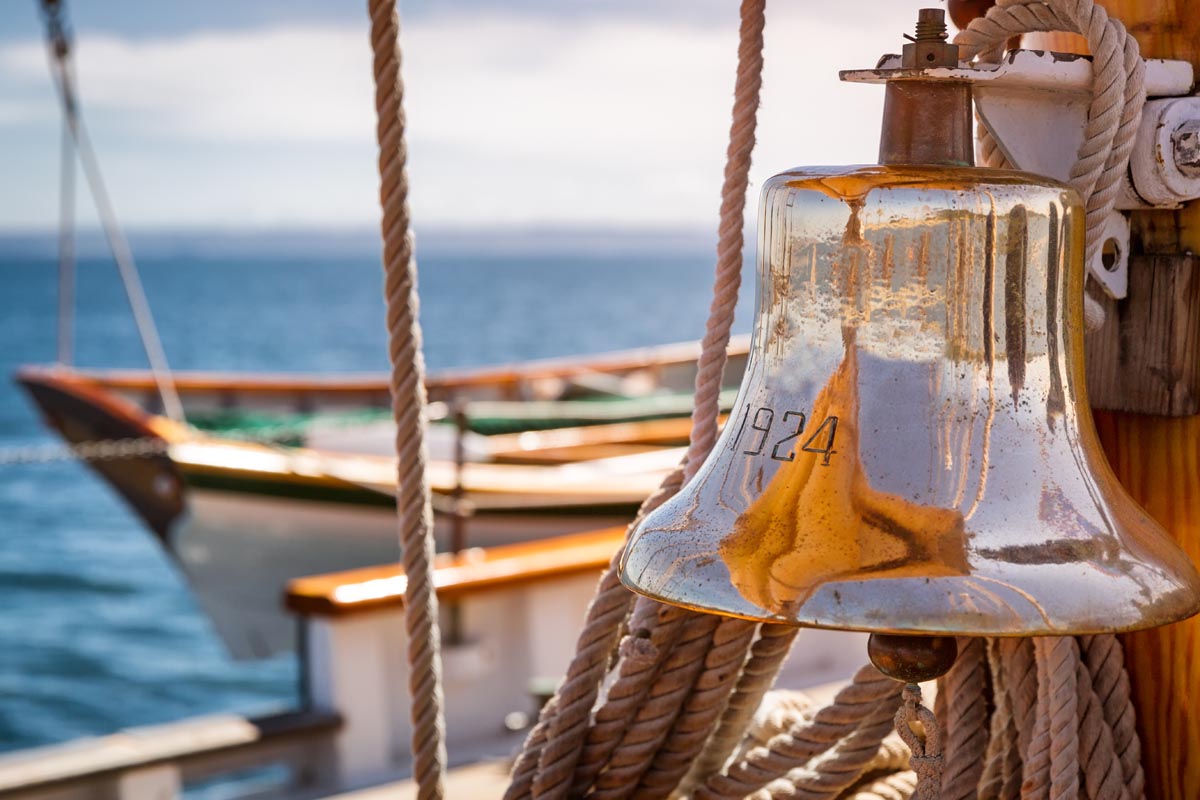 Brass ship bell on a classic sailboat at sea. Close up of the shiny bell reflecting the sails - ILTM_370770482 Brass ship bell on a classic sailboat at sea. Close up of the shiny bell reflecting the sails - ILTM_370770482